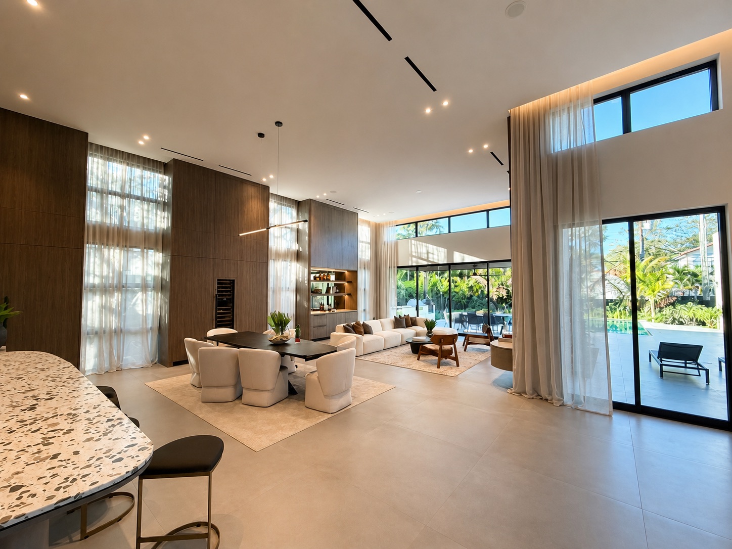 Open-plan living and dining with sheer curtains opening to a pool